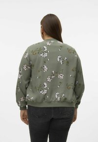 Grøn sweatshirt med blomsterprint og lange ærmer samt ribbede manchetter, der har lyserøde og hvide blomster mod en tekstureret baggrund.