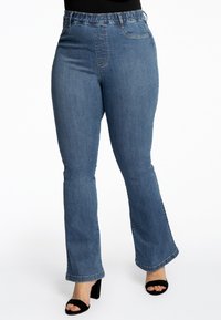 Jean en denim bleu évasé avec une taille élastique et des poches avant, présentant une texture lisse et une finition délavée.