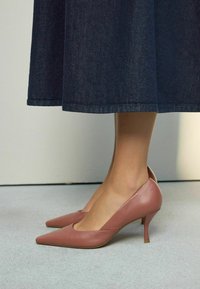 Decolleté in morbida pelle rosa con tacco a stiletto sottile e un'apertura a forma di V sui lati, abbinati a una gonna in denim scuro.