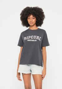 Szürke póló, amelyen vastag fehér betűkkel a "Rip Curl Australia" felirat látható, sima textúrával, világos farmer rövidnadrággal párosítva.