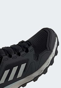 Chaussure de sport noire avec dessus en mesh, trois bandes réfléchissantes sur le côté, semelle blanche épaisse et texturée, lacets noirs.