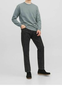 Jasnozielona bluza z okrągłym dekoltem, zestawiona z ciemnoszarymi jeansami. Model nosi czarne zamszowe buty z gumowymi podeszwami.