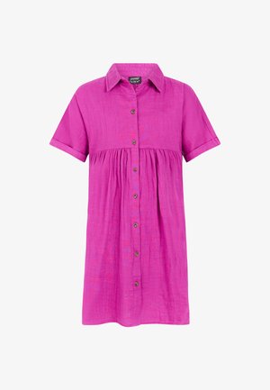 Robe chemise fuchsia à manches courtes, taille froncée et coupe ample. Portée avec des tongs noires et des bracelets colorés à un poignet.