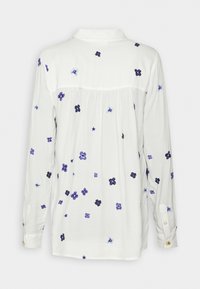 Blouse blanche à manches longues avec des imprimés floraux bleu foncé et bleu clair dispersés dans le dos et sur les manches, avec des poignets boutonnés et un col.