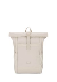 Beige roll-top backpack with front pocket, side mesh pockets, a central strap with buckle, and a small rectangular brand label on front.