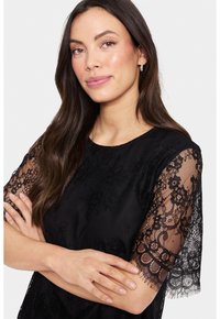 Black dress featuring intricate lace sleeves, a round neckline, and a textured body. The lace displays floral patterns with scalloped edges.