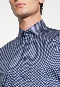 Camicia a motivo blu navy con design geometrico, chiusura con bottoni abbinati e colletto classico. Tessuto morbido.