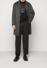 Abrigo de lana gris, sudadera negra con impresión de dibujos animados, pantalones negros, zapatos negros. Presenta un silueta entallada y un look en capas.