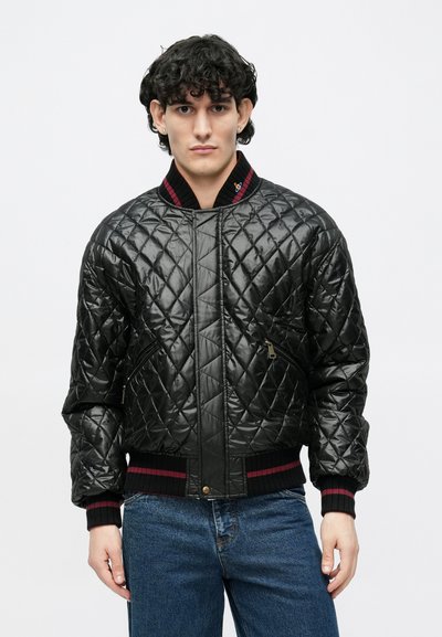 Čierna prešívaná bomber bunda s rebrovaným golierom a manžetami, s červenými akcentovými pruhmi a bočnými vreckami so zipsom. Hladký, lesklý materiál.