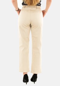 Pantaloni beige a gamba larga con tasche posteriori, una vita strutturata e abbinati a tacchi alti neri. Il tessuto ha una finitura liscia.