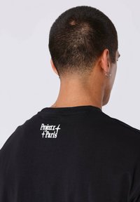 Camiseta negra de manga corta con un diseño gráfico de texto blanco en la parte posterior, hecha de material de algodón suave y de ajuste relajado.