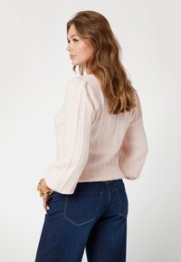 Maglione a coste di un delicato rosa, con maniche a palloncino, abbinato a jeans di denim blu scuro. Tessuto morbido con una vestibilità rilassata.