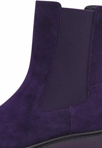 Bottine en daim violet avec des panneaux latéraux en élastique et une semelle noire lisse. La texture est douce et le design est élégant et moderne.