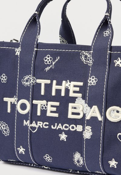 Geantă de pânză bleu marin cu modele florale și stele albe, având text brodat alb "THE TOTE BAG MARC JACOBS".
