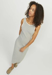Abito maxi senza maniche a righe bianche e nere. Tessuto morbido e elastico con un corpino aderente e una gonna larga. Indossato con zoccoli casual color cammello.