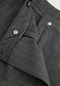 Szare spodnie w prążki z gładką fakturą, zapinane na srebrny guzik, z wewnętrzną kieszenią na zamek. Widoczne szwy.