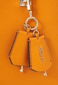 Pomarańczowa torebka z fakturowaną powierzchnią, srebrnym okuciem oraz dwoma brelokami z logo "GUESS".