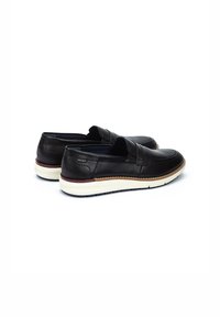 Zapatos negros de piel tipo deslizante con una textura suave, suela blanca acolchada y detalle en marrón a lo largo del borde. Sin marcas visibles.