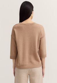 Brauner, gestrickter Pullover mit einem gerippten Halsausschnitt und hochgekrempelten Dreiviertelärmeln. Weiche Textur, lockere Passform und ein leicht verkürzter Saum.