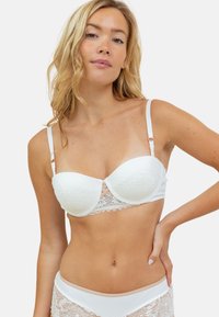 Soutien-gorge blanc avec armatures, recouvert de dentelle, avec des bretelles réglables, des bords festonnés et un design distinctif au centre. Tissu texturé avec une finition lisse.