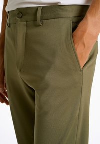 Khaki broek met een gladde textuur, voorzien van schuin geplaatste zijzakken en een knoopsluiting in de taille. Getailleerde pasvorm en eenvoudig ontwerp.