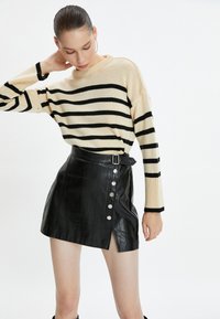 Sweter w paski w kolorze kremowym i czarnym, zestawiony z czarną mini spódnicą z faux skórki z zatrzaskami i bocznym rozcięciem.