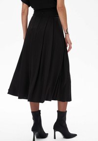 Zwarte, geplooide midi-rok met een hoge taille en verborgen rits. Zachte, vloeiende stof met een gladde textuur, gecombineerd met elegante zwarte enkellaarsjes.