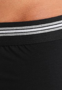 Schwarzer Stretchbund mit zwei horizontalen grauen Streifen oben, der in eine glatte Stoffstruktur darunter übergeht.