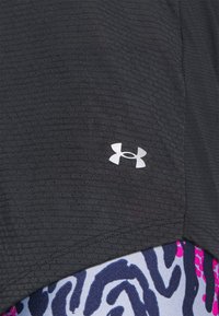Svart atletisk tyg med ett texturerat mönster som har en vit Under Armour-logotyp, lager på lager över en färgglad djurtryckad botten.
