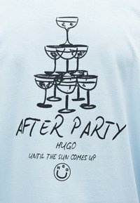 Στοίβα από εννέα ποτήρια σαμπάνιας σε σχήμα πυραμίδας με το κείμενο «AFTER PARTY HUGO UNTIL THE SUN COMES UP» και λογότυπο με χαμογελαστό πρόσωπο από κάτω.