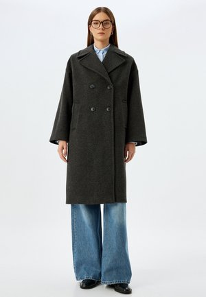 Dunkelgrauer, doppelt geschnittener Wollmantel mit großen Revers, seitlichen Taschen und gerader Silhouette, getragen über hellblauen, weit geschnittenen Jeans.