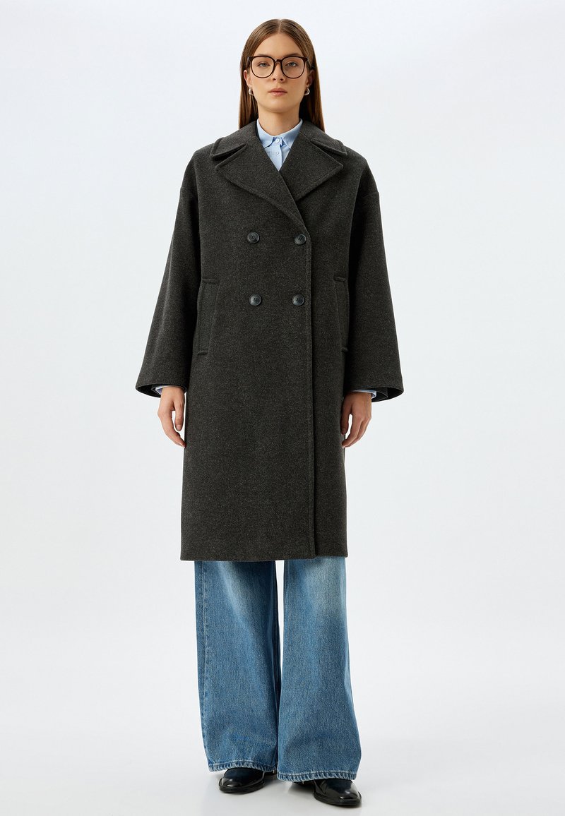Tweekleurige, donkergrijze wollen jas met grote notch-lapels, zijzakken en een rechte snit, gedragen over lichtblauwe denim wijdpantalons.