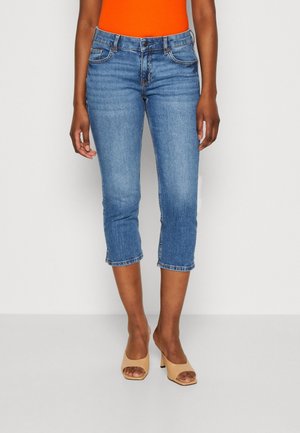 Jean capri en denim bleu avec une taille mi-haute, un design à cinq poches et un ourlet arrivant au milieu du mollet, associés à des sandales à talons nude.