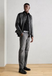 Zwarte leren jack over een zwart shirt, grijze jeans en zwarte chelsea boots. De outfit heeft een getailleerd ontwerp en subtiele texturen.