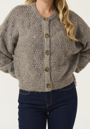 Femme portant un cardigan gris tricoté à boutons avec un motif texturé et un jean taille haute bleu foncé.