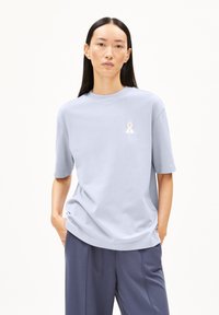 Lichtblauwe katoenen t-shirt met korte mouwen, ronde halslijn en witte geborduurde lintdetails op de borst. Verkrijgbaar met een relaxte pasvorm.