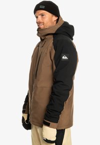 Braune und schwarze isolierte Jacke mit Kapuze, ausgestattet mit einem Reißverschluss, elastischen Bündchen und einem Logo-Patch am Ärmel; strukturierter Stoff.