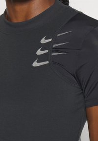 Camiseta deportiva negra de manga corta, con logotipos de Nike en gris reflectante y una tela texturizada. Vista en primer plano del área del hombro y el cuello.