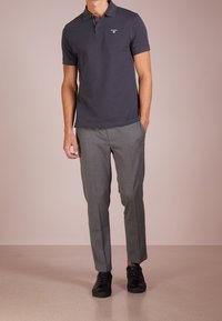 Polo shirt pour homme gris foncé à manches courtes, associé à un pantalon ajusté gris clair et des baskets noires à lacets. Détail logo simple sur le shirt.