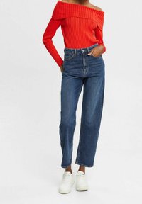 Haut rouge en tricot côtelé à épaules nues associé à un jean en denim bleu taille haute et à des baskets blanches, mettant en avant une silhouette décontractée et ajustée.
