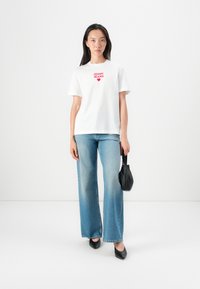 White cotton t-shirt featuring red "JOOP! JEANS" text and heart graphic, paired with light blue wide-leg jeans and black pointed shoes.
