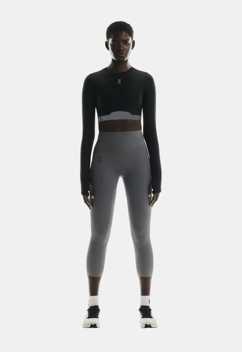 Mustmustri mustsleeve crop top koos kõrge vöökohaga hallide leggidega, mõlemad omavad stiilset disaini. Sisaldab logo aktsente ja sujuvat ehitust.