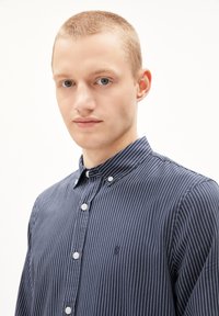 Marineblaues Hemd mit weißen vertikalen Streifen, leichtes Material, Kragen und kleinem Logo auf der Brust. Eng anliegendes Design.