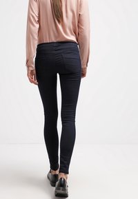 Tummansiniset skinny-farkut korkealla vyötäröllä ja takataskuilla, yhdistettyinä vaaleanpunaiseen pitkähiharaiseen puseroon ja mustiin kenkiin.