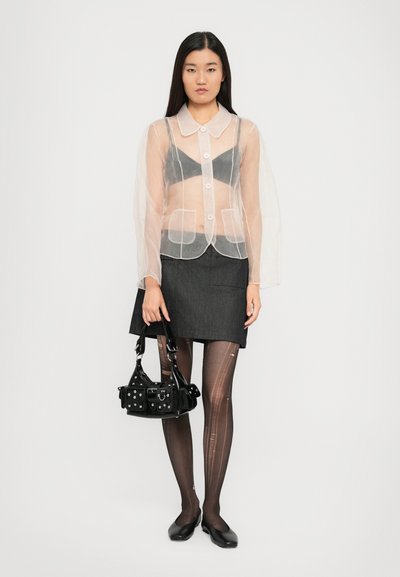 Läbipaistev eeslik, must rinnahoidja all, hall seelik, mustade mustritega sukkpüksid, narmastega must kott ja mustad plätud.