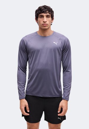 Mann, der nach vorne blickt, trägt ein graues langärmeliges Sportshirt und schwarze Shorts mit Puma-Logos auf beiden.