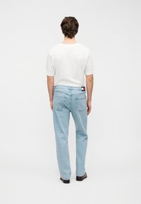 Ανοιχτό μπλε τζιν παντελόνι με ευθε ία γραμμή, διαθέτει πίσω τσέπες και ετικέτα με αντίθετο χρώμα της μάρκας στη μέση. Συνοδεύεται από λευκό μπλουζάκι.