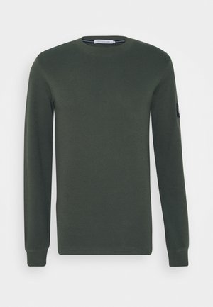 Dunkelgrüner Pullover mit Rundhalsausschnitt und langen Ärmeln, gerippten Bündchen und Calvin Klein Jeans Label am linken Ärmel.