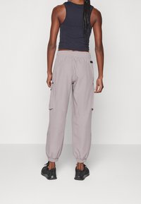 Vaaleanharmaat cargo-housut, joissa on elastiset hihnat ja taskut, yhdistetty mustaan istuvaan toppiin ja mustiin lenkkareihin. Sileä pinta ja rento muotoilu.