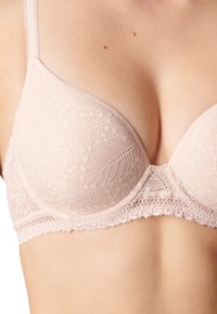 Soutien-gorge en dentelle rose clair avec un design de coque lisse et moulé, orné de motifs en dentelle décorative et de bords festonnés le long de la bande et des bretelles.